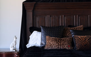 Collection of pillows by Loren Estes Sable, Muse, and Relic on a large wooden bed with a black velvet duvet cropped image