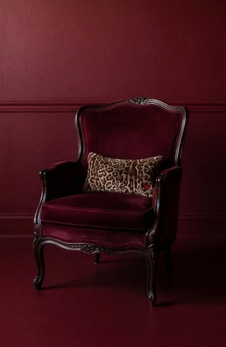 Muse by Loren Estes sits in a vintage red velvet chair in a color drenched red room